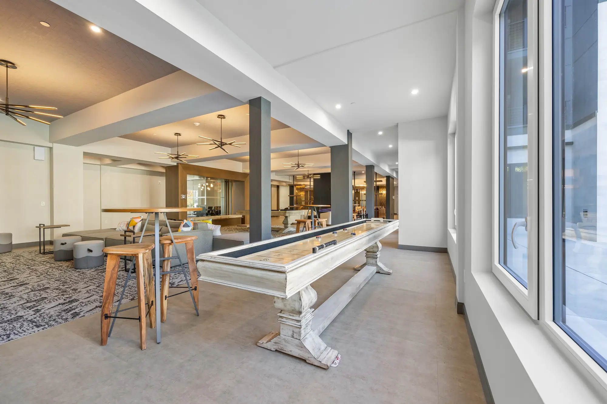 The Beacon clubhouse lounge and game room with couches, high top bar tables, shuffleboard, and a billiards table