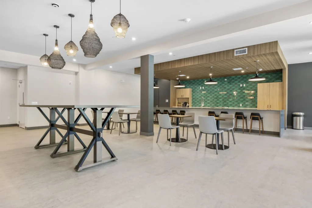 The Beacon clubhouse community kitchen and dining area with extra long bar top counter, bar stool seating, dining tables for two, and a standing table