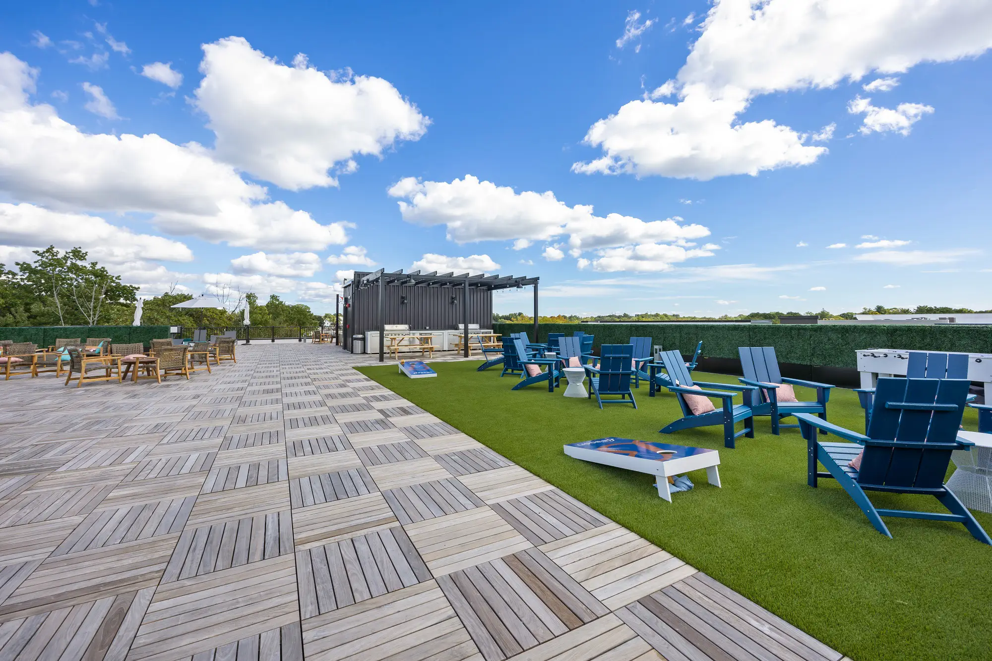 The Beacon rooftop game lawn and grill area with pergola covering, corn hole, foosball, and patio chairs