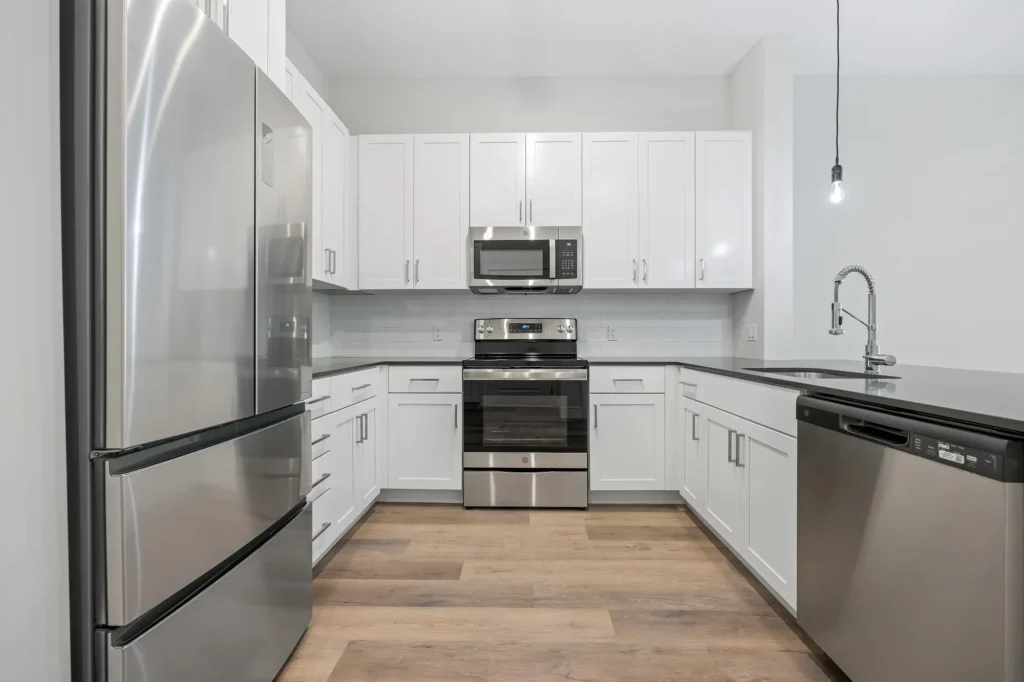 The Beacon apartment home u-shaped kitchen with white cabinets, black countertops, undermounted sink, wood flooring, and stainless steel appliances