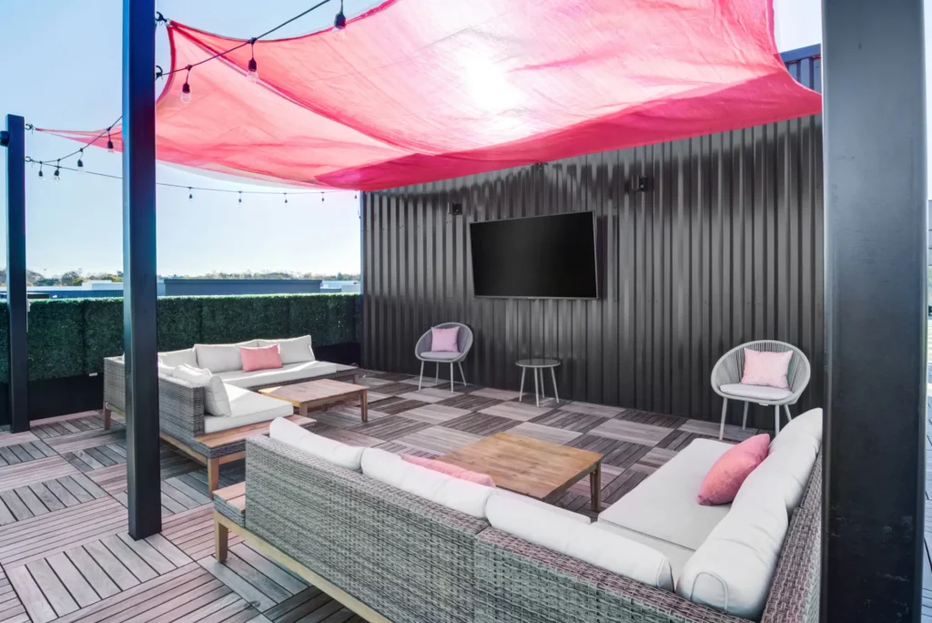 The Beacon rooftop deck with patio sectional couches, chairs and a wall mounted tv all covered by handing sheet and lights