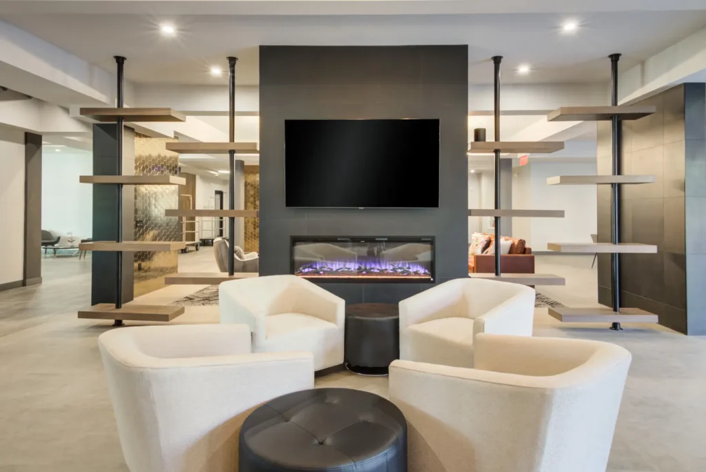 The Beacon clubhouse lounge with chairs, an in-wall fireplace, and wall mounted tv
