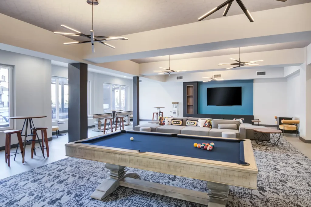 The Beacon game room lounge with billiards table, shuffleboard, arcade table, couches, high top tables, and a wall mounted tv