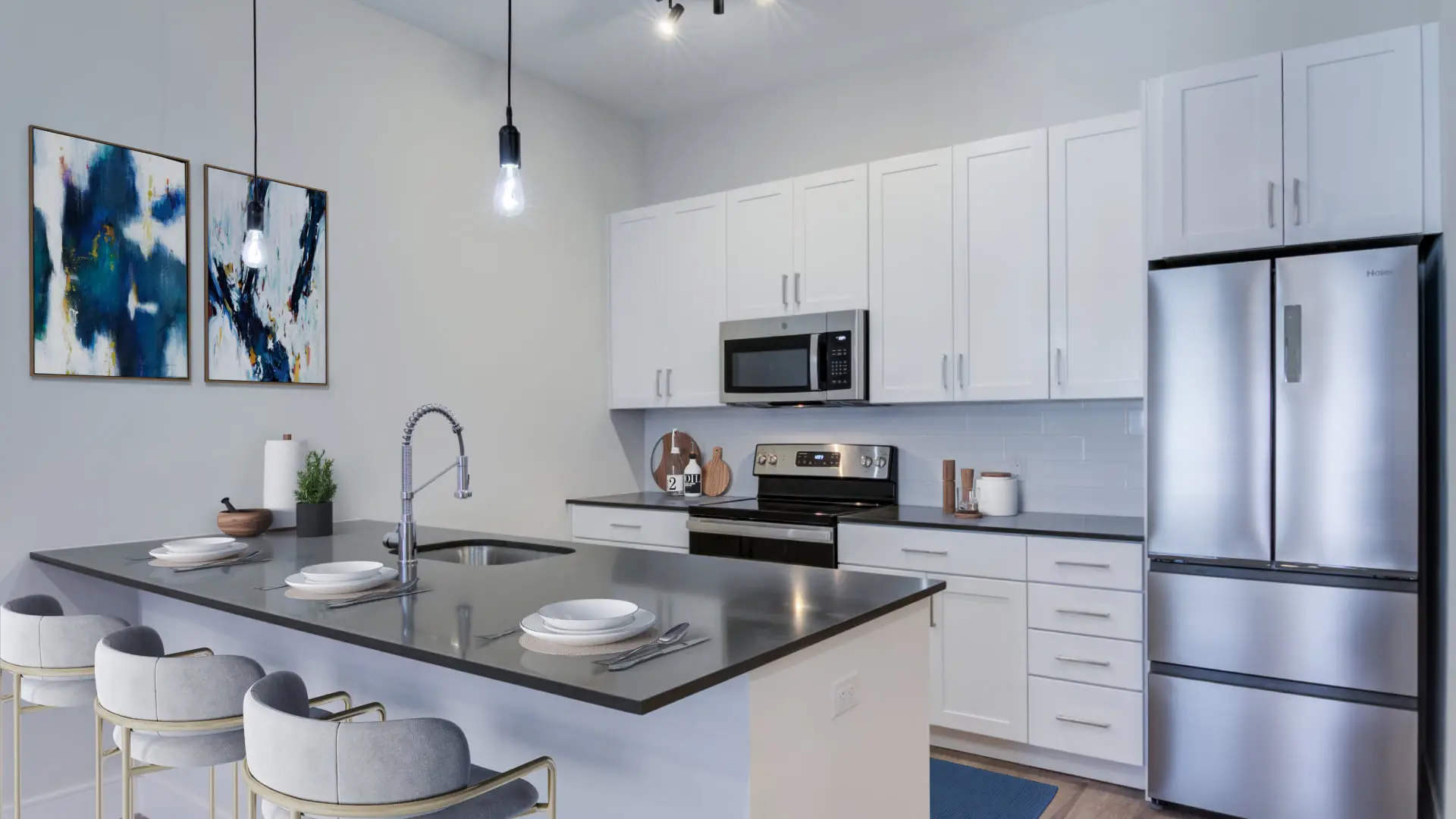 The Beacon furnished apartment kitchen close up with white cabinets, a peninsula style black countertop with bar stool overhang, undermounted sink, and stainless steel appliances